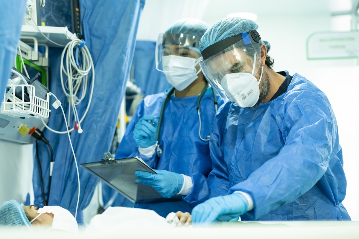 Pair of doctors checking an inpatient in intensive care while wearing their biosecurity suits