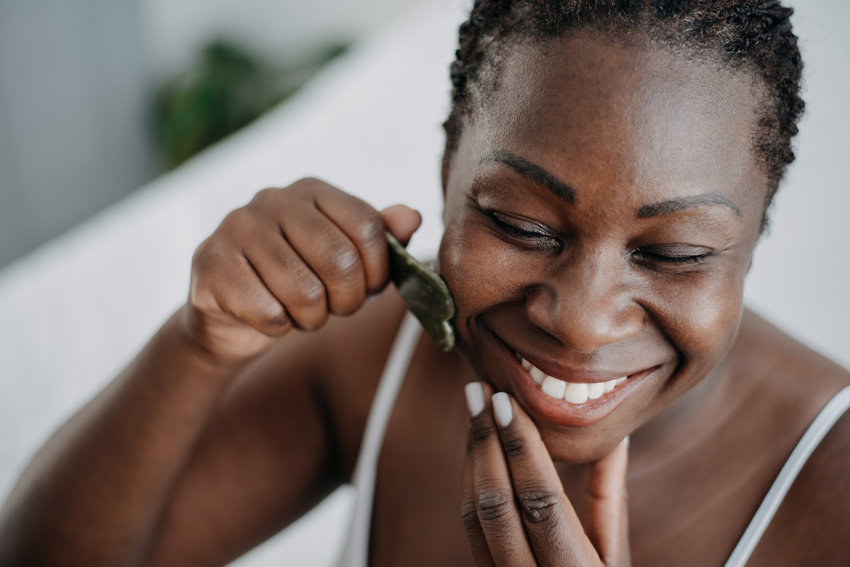 Close up of a smiling woman using a gua sha tool on her face