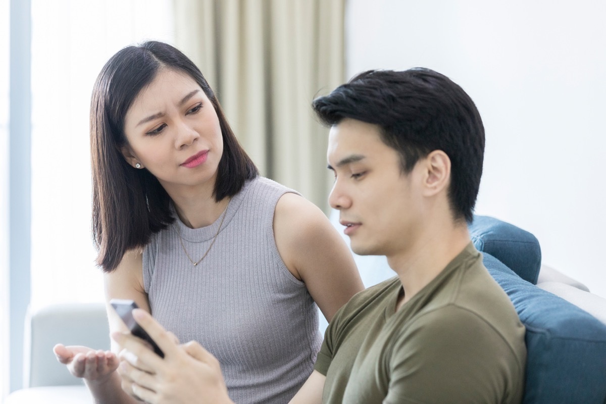 asian woman looking annoyed while asian man ignores her to look at phone