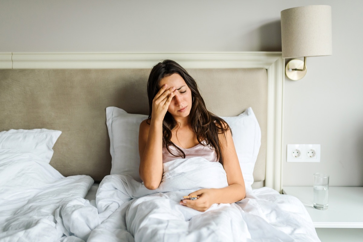 woman lying in bed, feeling unwell, with her hand on her head. Sickness / illness concept. Coronavirus / fever / headache concept. Home isolation.