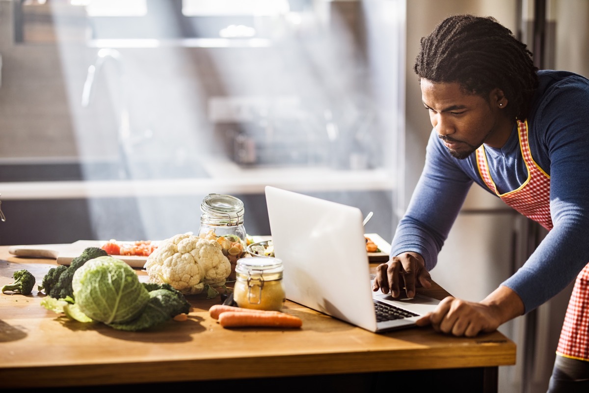 man using laptop while searching for the right lunch recipe in the kitchen.