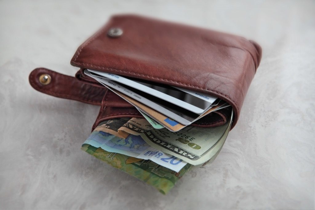 we see a brown leather wallet over packed with different currency and credit cards on a pale marble surface