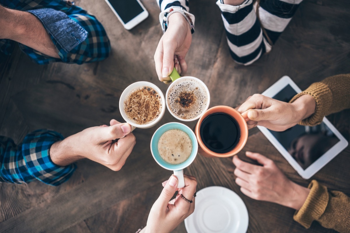 Close up from above of friends clinking coffee cups together