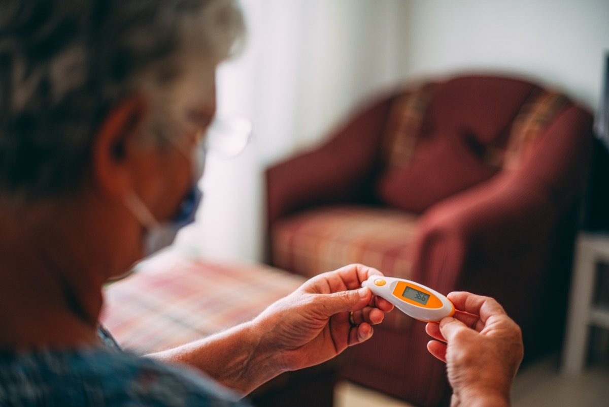 Mature Woman With Mask Measuring Her Temperature With Medical Digital Thermometer