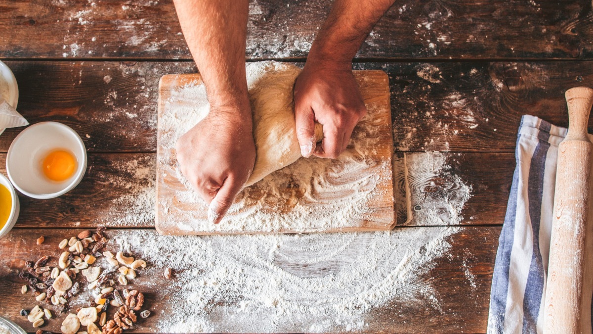 Bakery business. Culinary art. Chef kneading dough. Top view of hands working. Rolling pin and flour on wooden table.