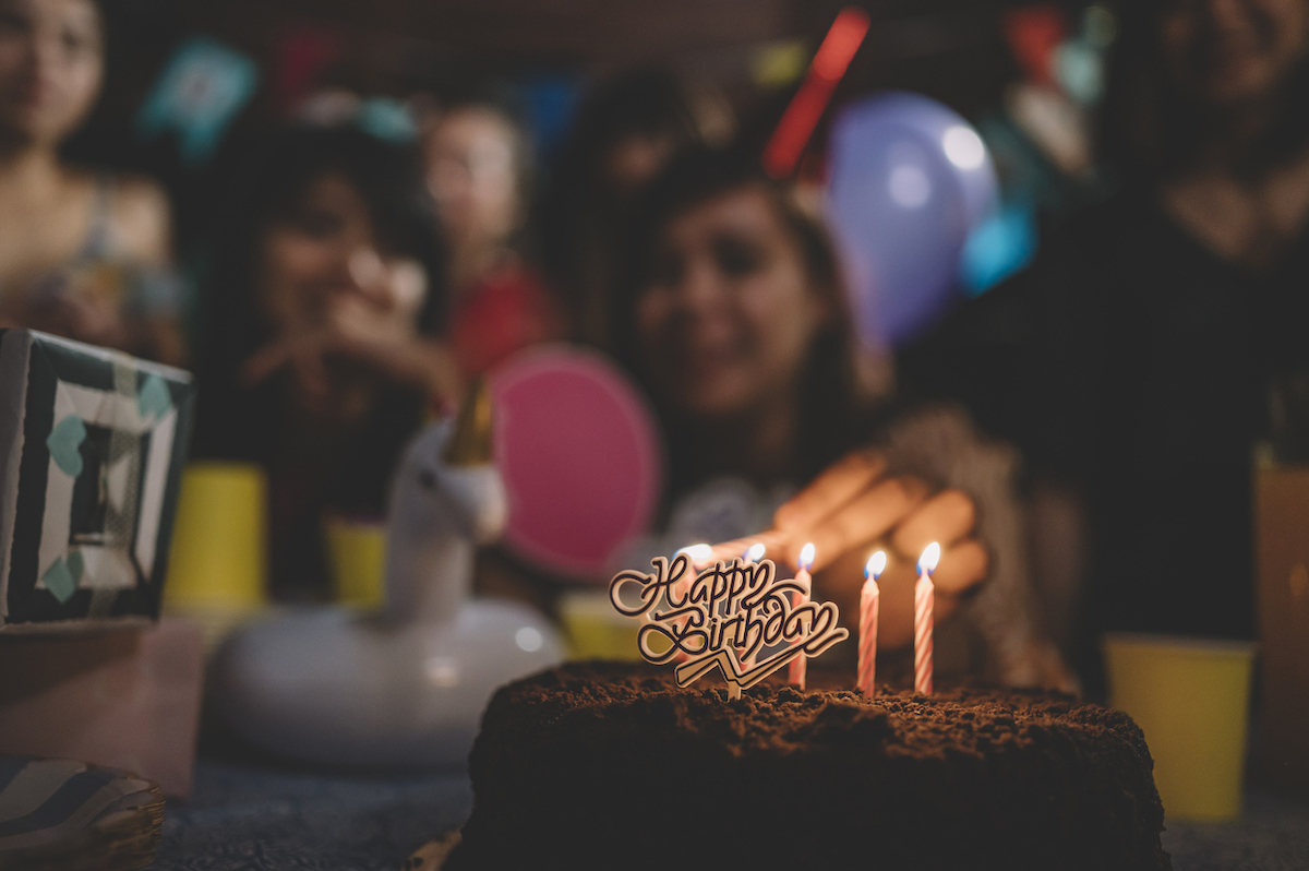 a group of friends gathering together celebrating birthday at night, lighting candles on cake