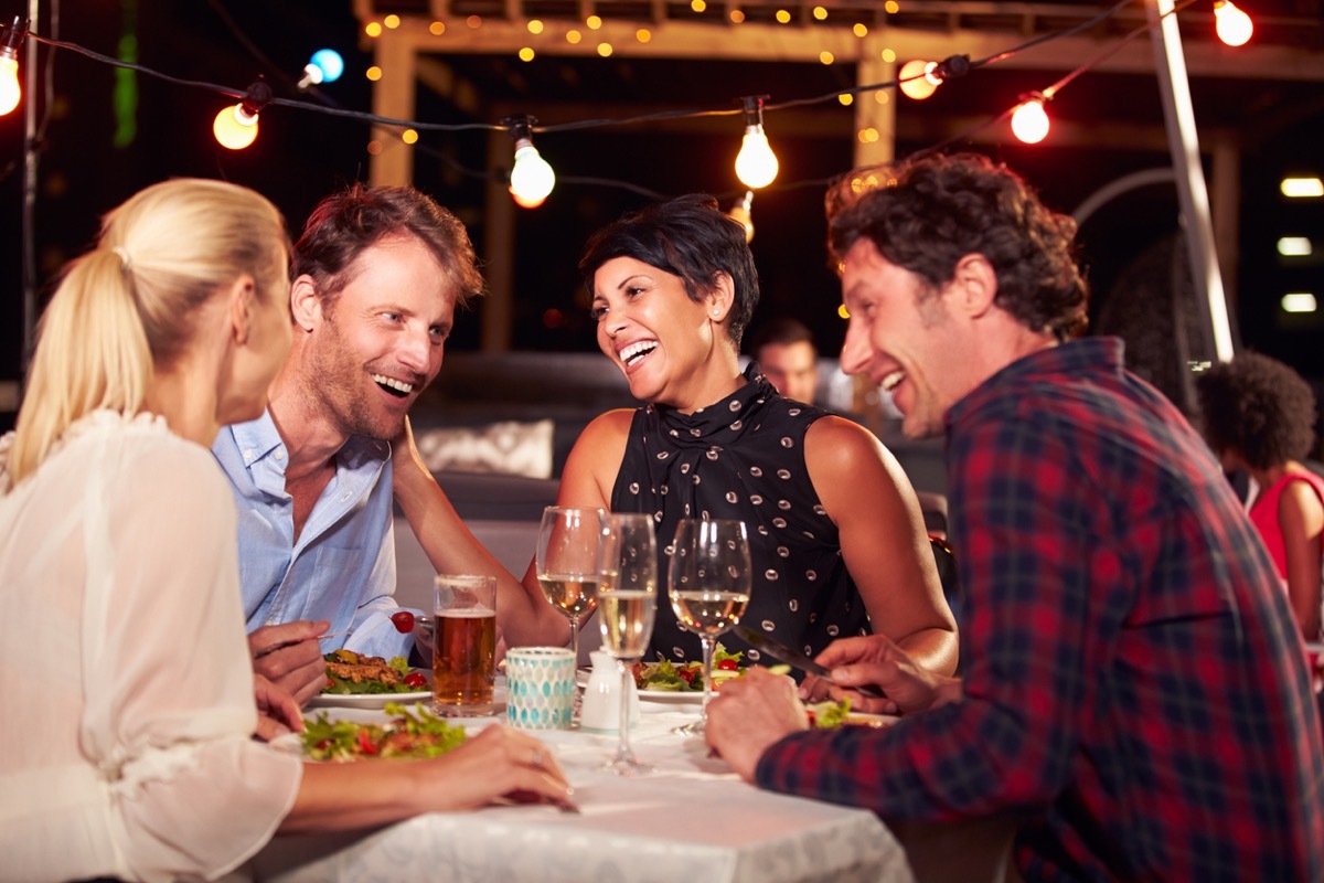 group of four friends having dinner on a rooftop patio at night