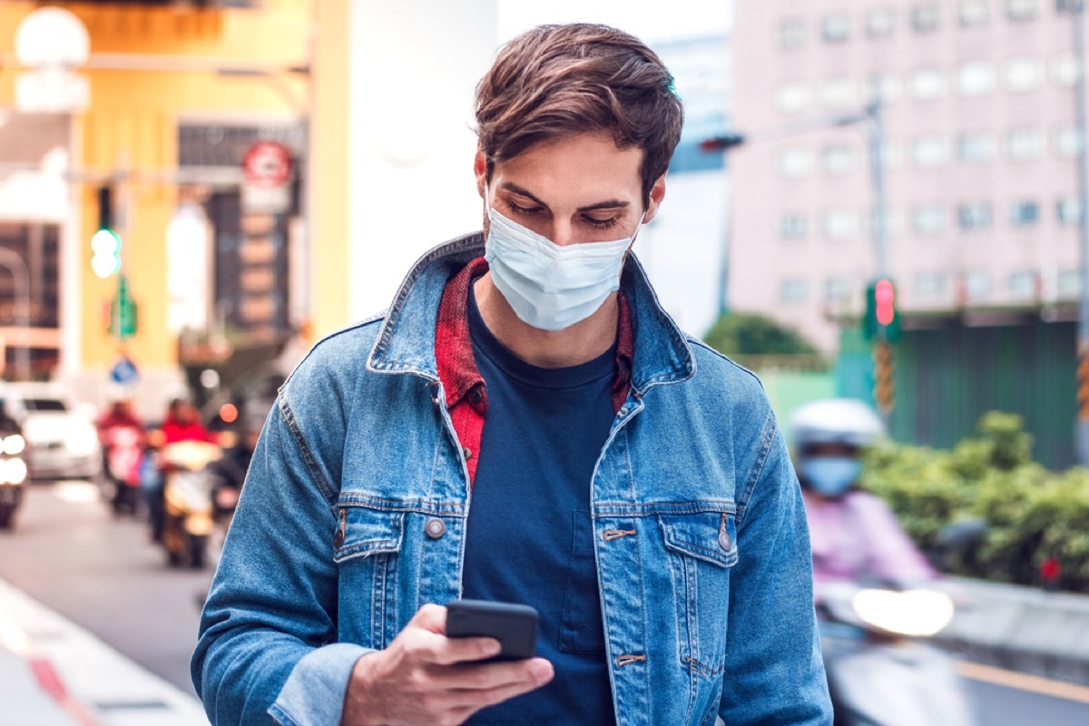 white man with face mask looking at his phone outside