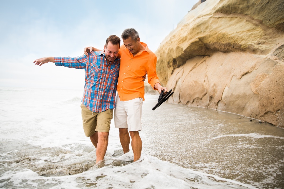 white man and asian man embracing and avoiding the waves on a beach