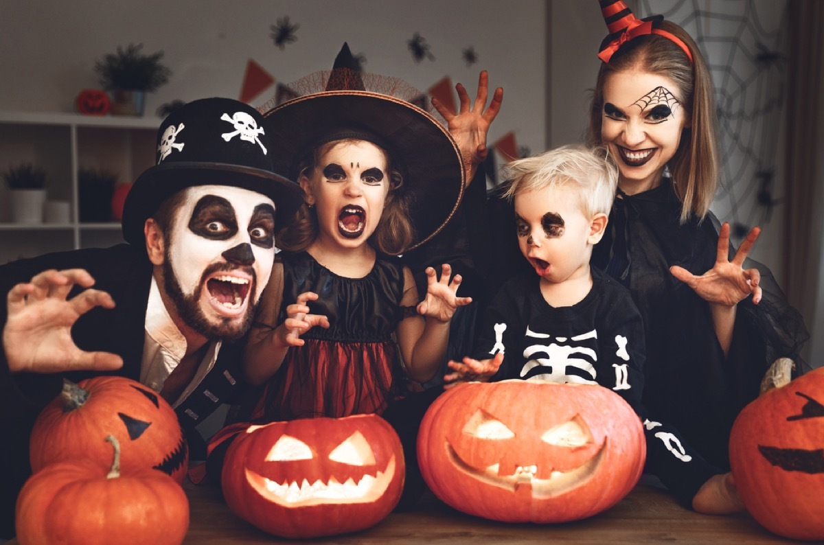 family in halloween costumes standing in front of jack o'lanterns