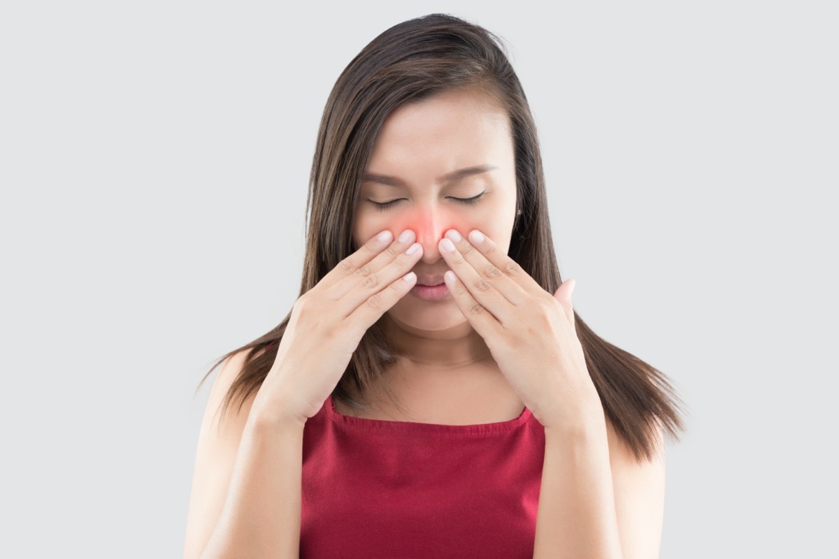 woman in red wear feeling unwell because of sinus against a gray background