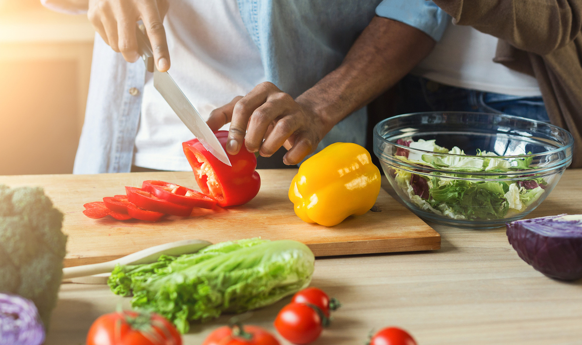 man of color cutting vegetables for healthy vegetarian salad in kitchen