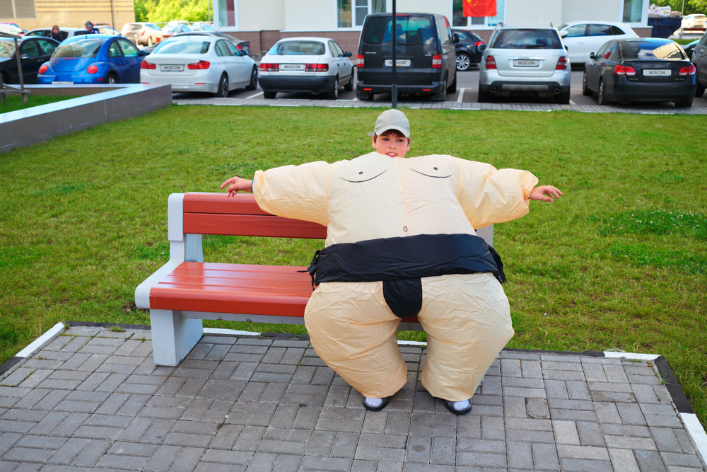 boy wears sumo wrestler inflatable fat suit halloween costume while sitting on bench