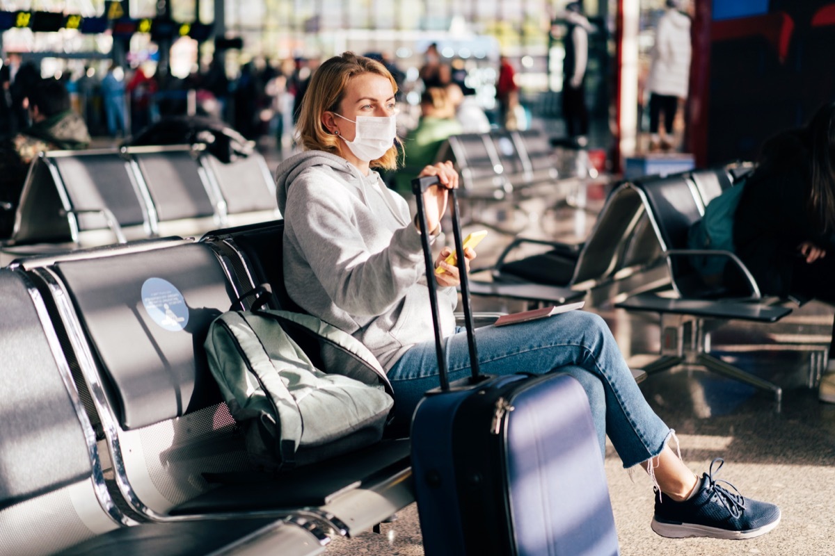 A female passenger in a medical mask is waiting for a flight at the airport.