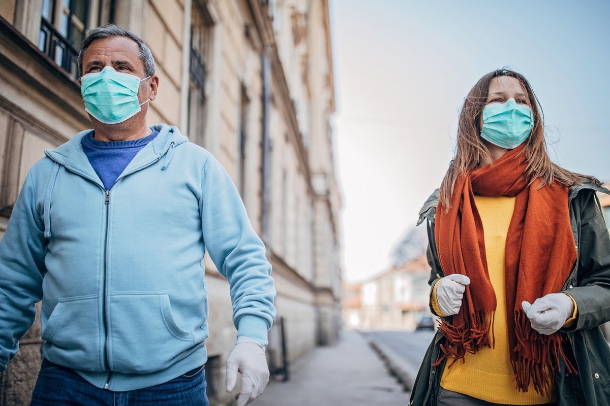 older white man and woman with masks walking outside